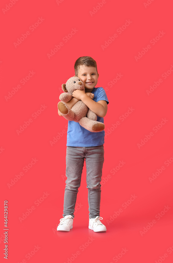 Cute little boy hugging teddy bear on red background