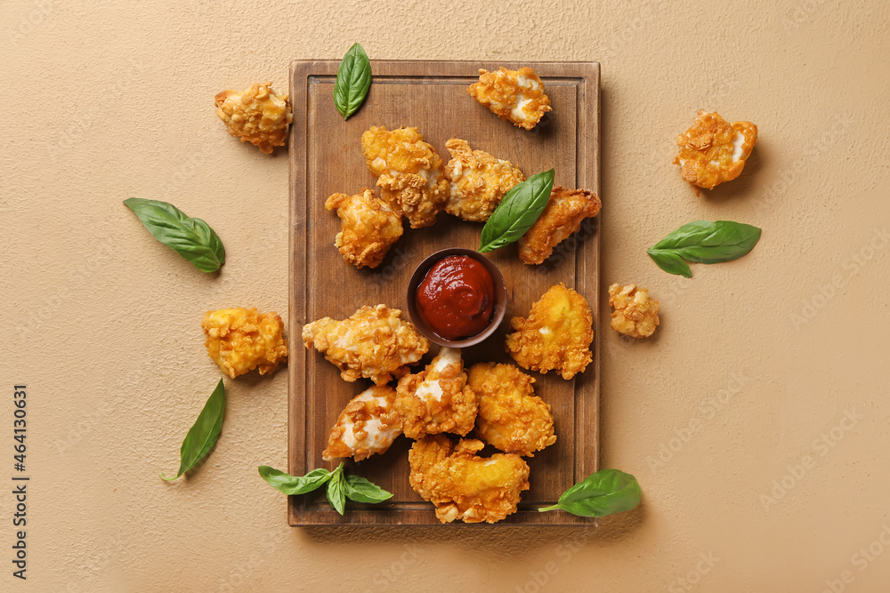 Board with tasty fried popcorn chicken, sauce and basil on color background