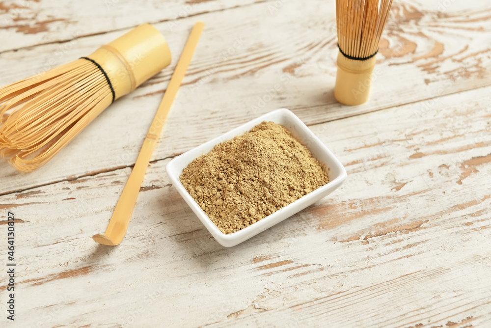 Bowl with hojicha powder, chasen and chashaku on white wooden background