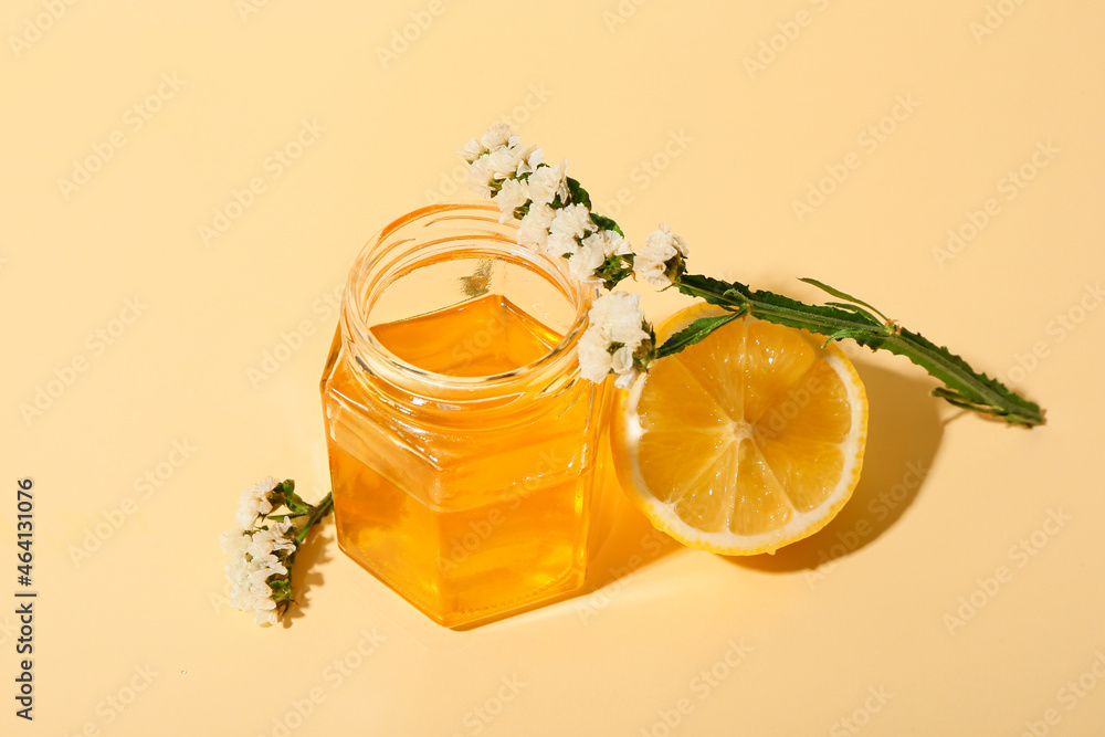 Jar of sweet honey, lemon and flowers on color background