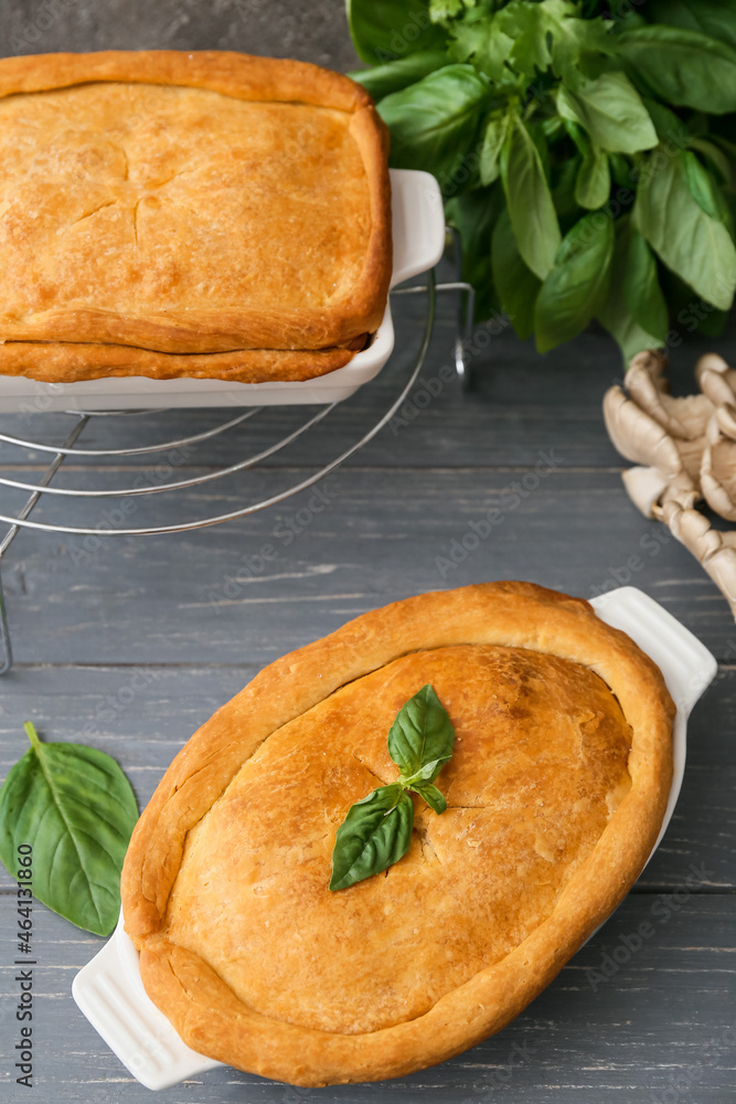 Baking dishes with tasty mushroom pot pie on grey wooden background