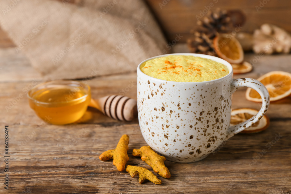 Cup of delicious turmeric latte on wooden background