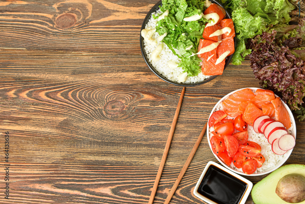 Tasty poke bowls with salmon, vegetables and sauce on wooden background