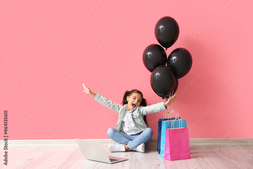 Happy little girl with laptop near pink wall. Black Friday sale