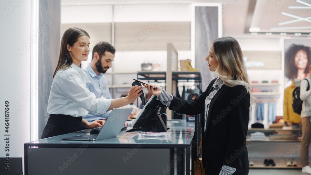 服装店：柜台上的年轻女人从友好的零售销售助理那里买衣服，支付智慧