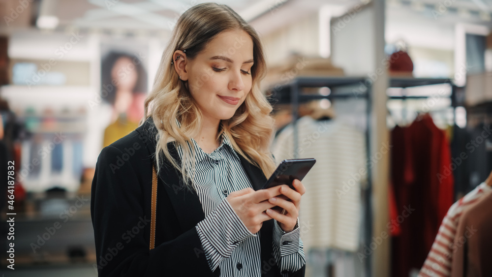 Beautiful Smiling Female Customer Shopping in Clothing Store, Using Smartphone, Browsing Online, Com