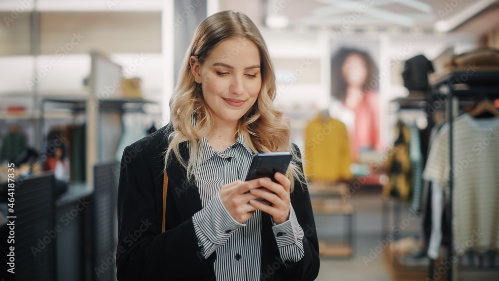 Beautiful Smiling Female Customer Shopping in Clothing Store, Using Smartphone, Browsing Online, Com