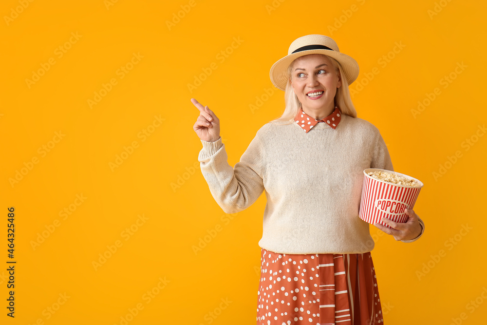 Mature woman with tasty popcorn pointing at something on color background