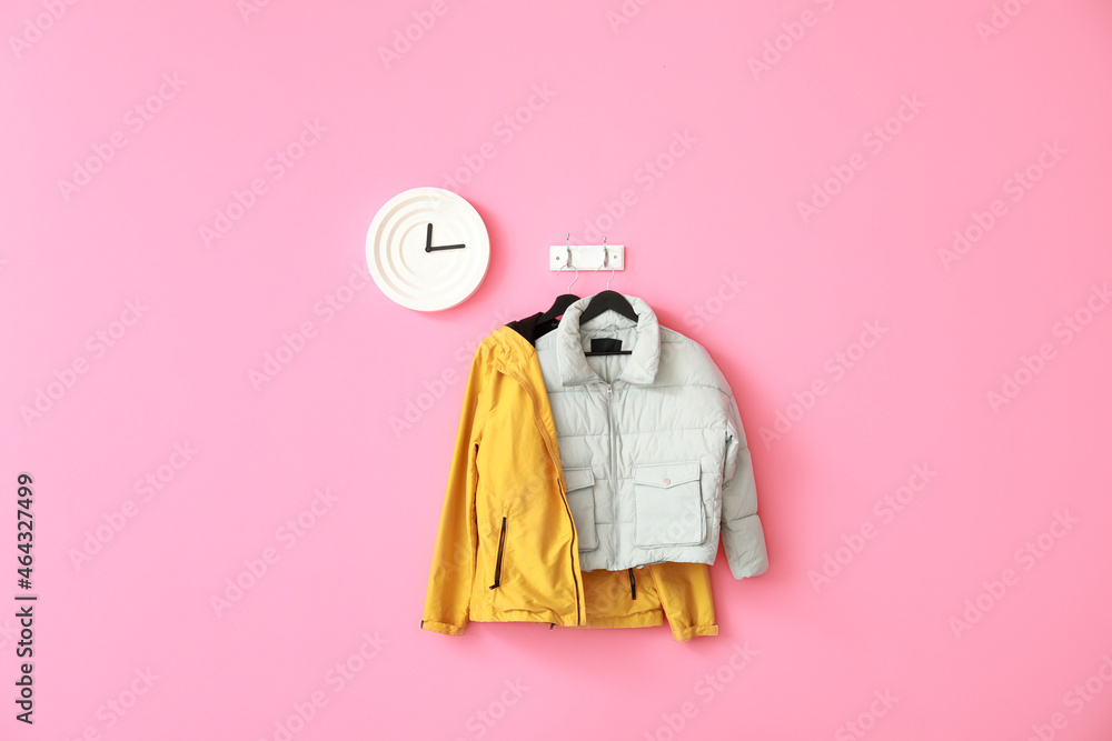 Stylish jackets and clock hanging on pink wall