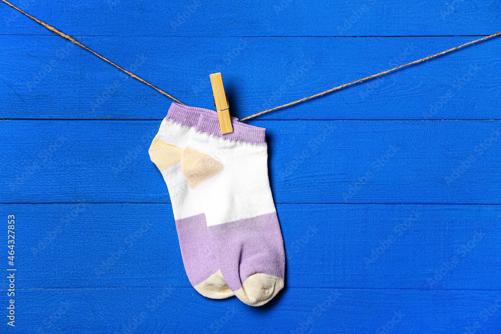 Pair of socks hanging on clothesline against color wooden background