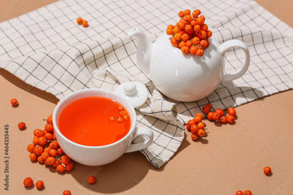 Composition with cup of tasty rowan tea, teapot and berries on color background