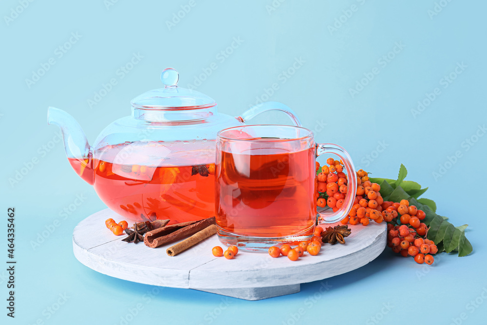 Board with tasty rowan tea, berries and spices on color background