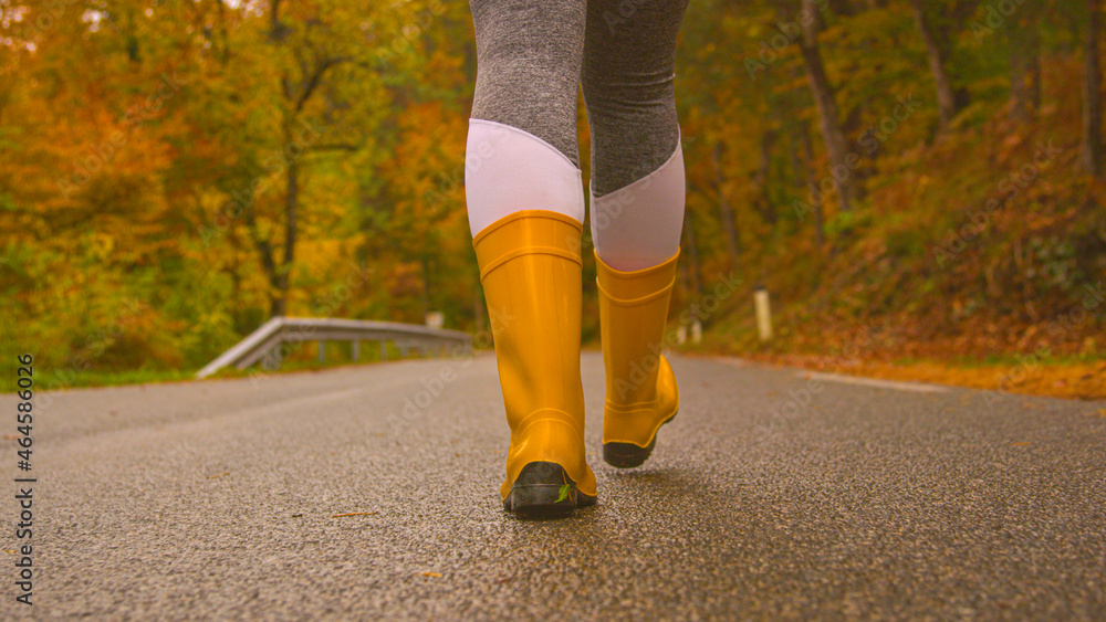 CLOSE UP: Female traveler wears rubber boots while walking down a forest route