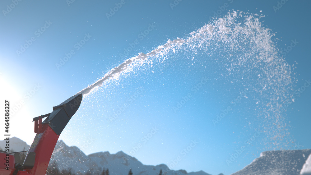 CLOSE UP: Detailed shot of a snowblower machine blowing snow into the sunny air.