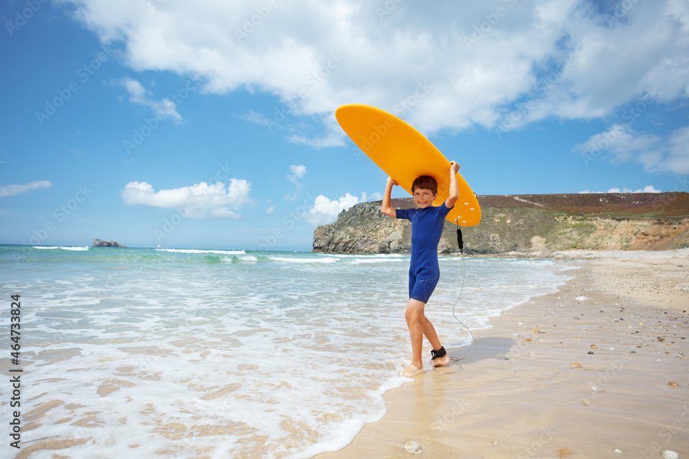 Boy in wetsuit pose with surfboard on sea