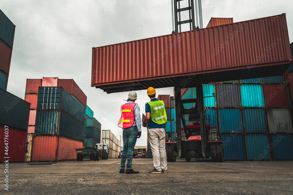 Industrial worker works with co-worker at overseas shipping container yard . Logistics supply chain 