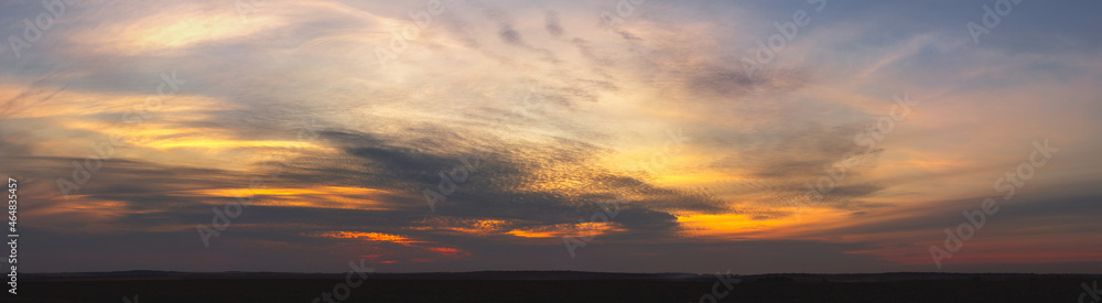 Sunset in orange tones with fluffy clouds and trees.