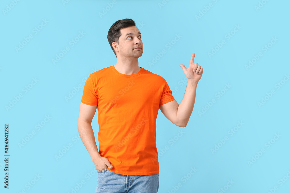 Handsome young man in stylish t-shirt pointing at something on color background