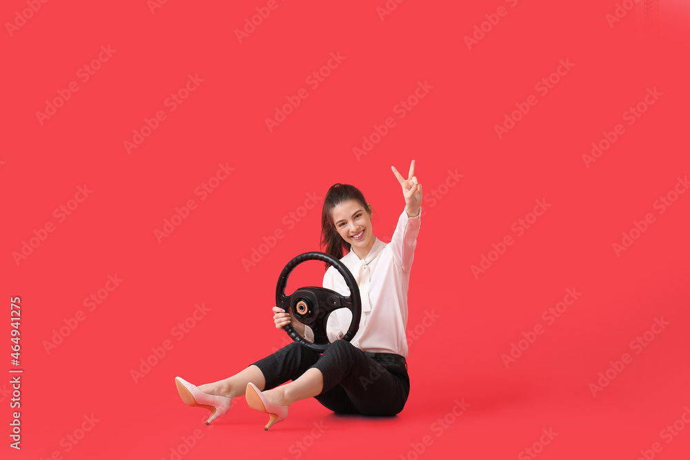 Young businesswoman with steering wheel showing victory gesture on color background