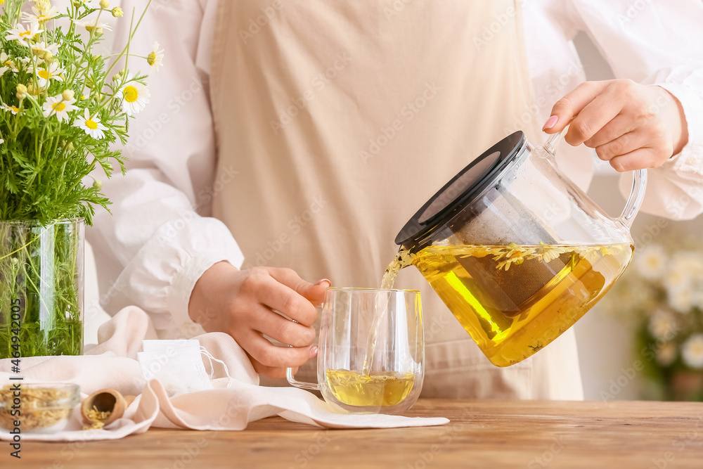 女人把美味的洋甘菊茶从茶壶里倒进桌子上的杯子里