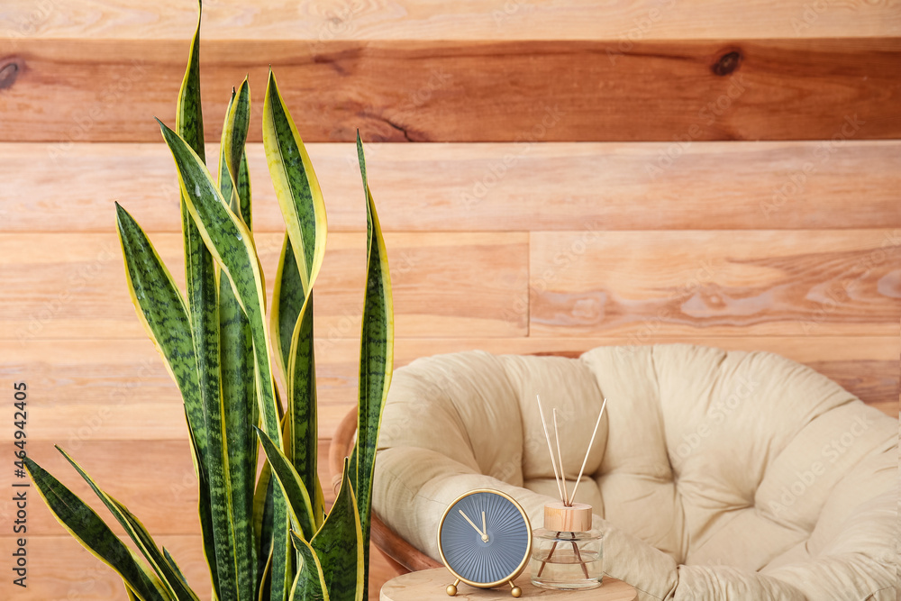 Table with alarm clock near comfy armchair and wooden wall