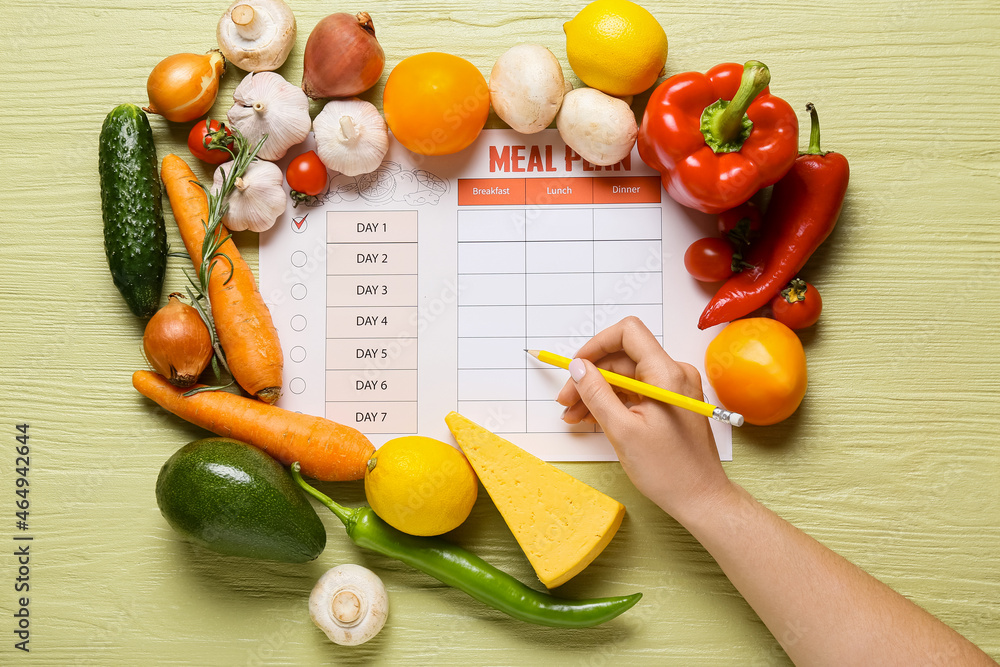 Woman making meal plan on color wooden background