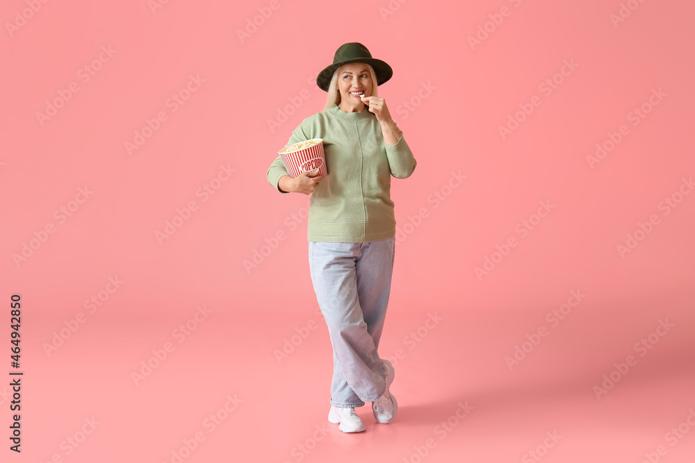 Mature woman eating tasty popcorn on color background