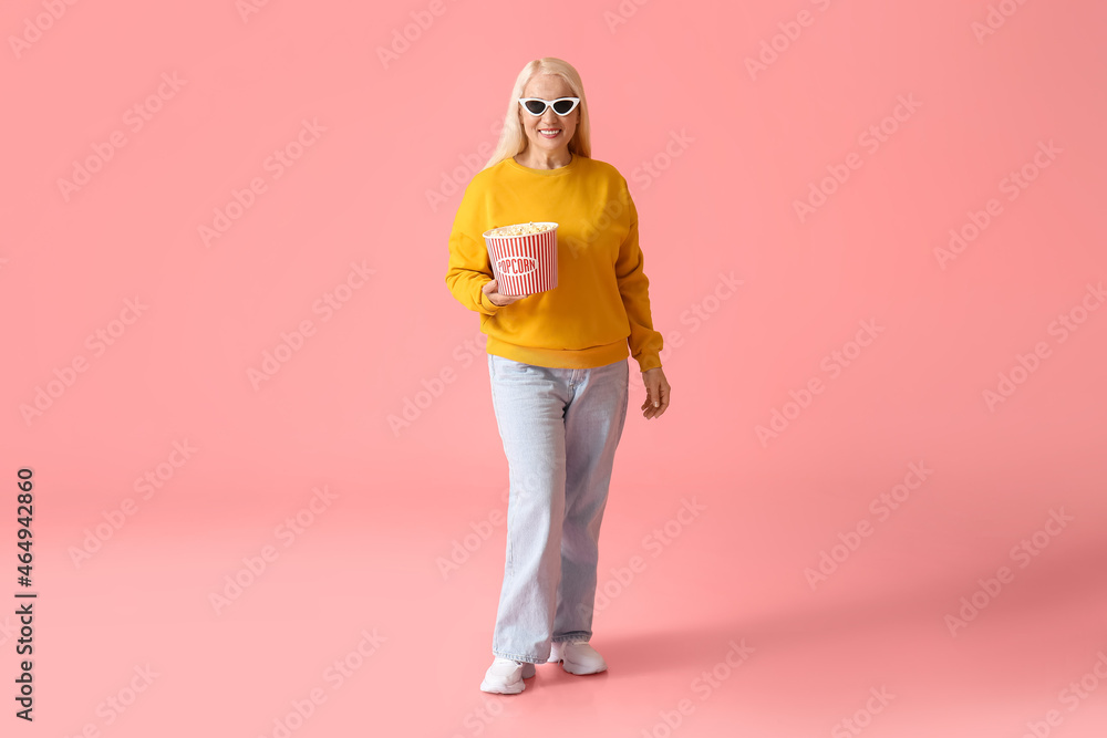 Mature woman with tasty popcorn on color background