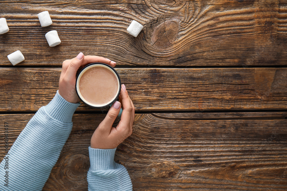 Woman adding marshmallow to cup of cacao on wooden background