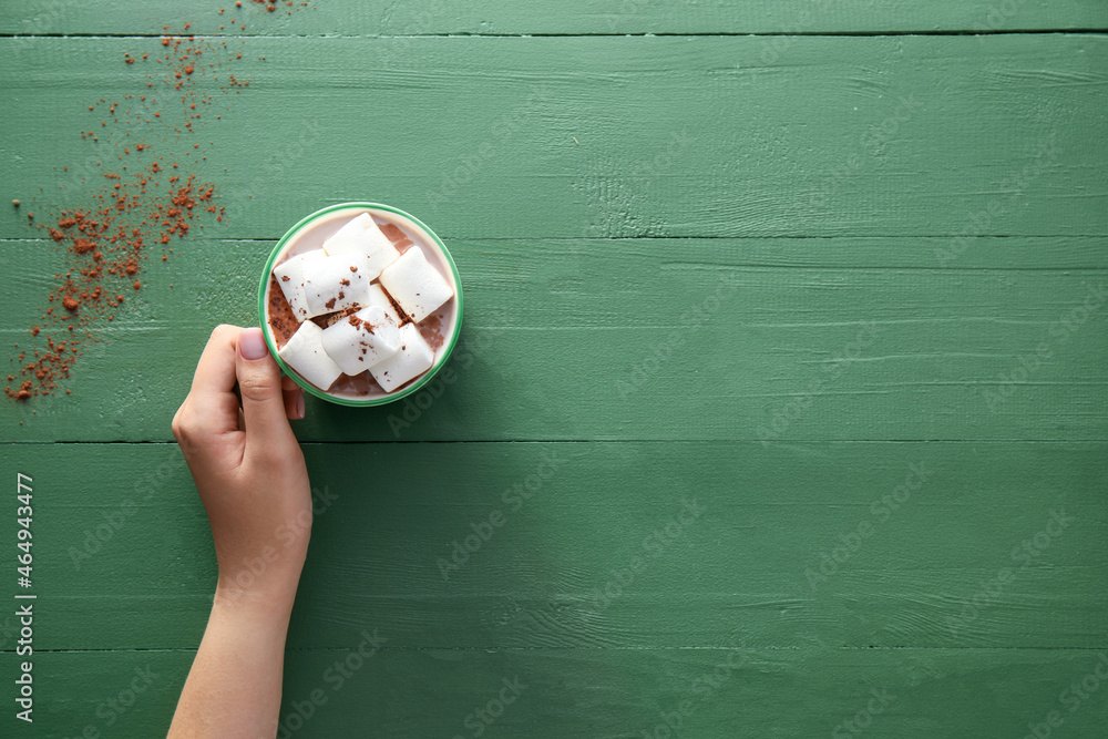 Female hand with cup of cacao on green wooden background