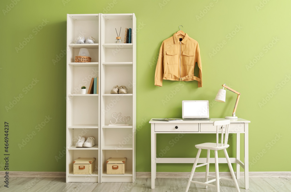 Modern workplace, shelving unit and yellow jacket hanging on green wall