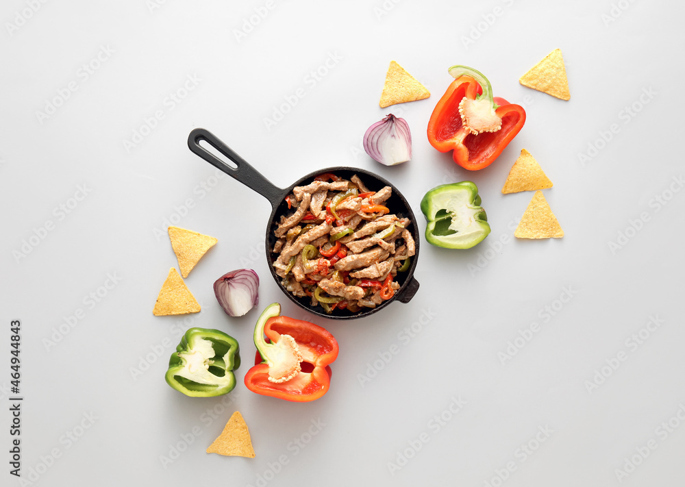 Frying pan with tasty beef Fajita, nachos and vegetables on white background