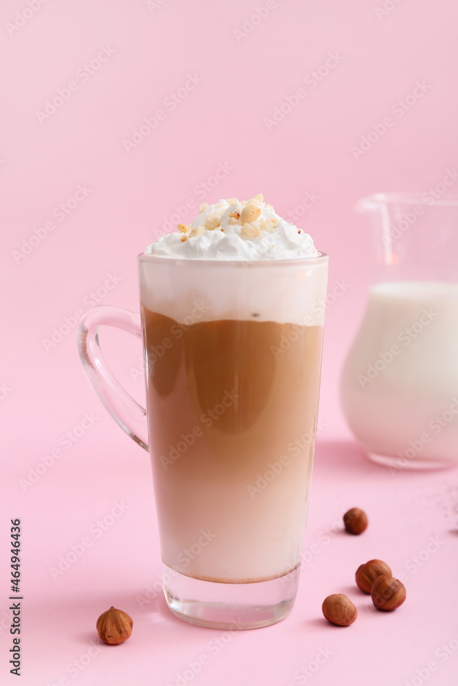 Glass cup of tasty latte with nuts on pink background