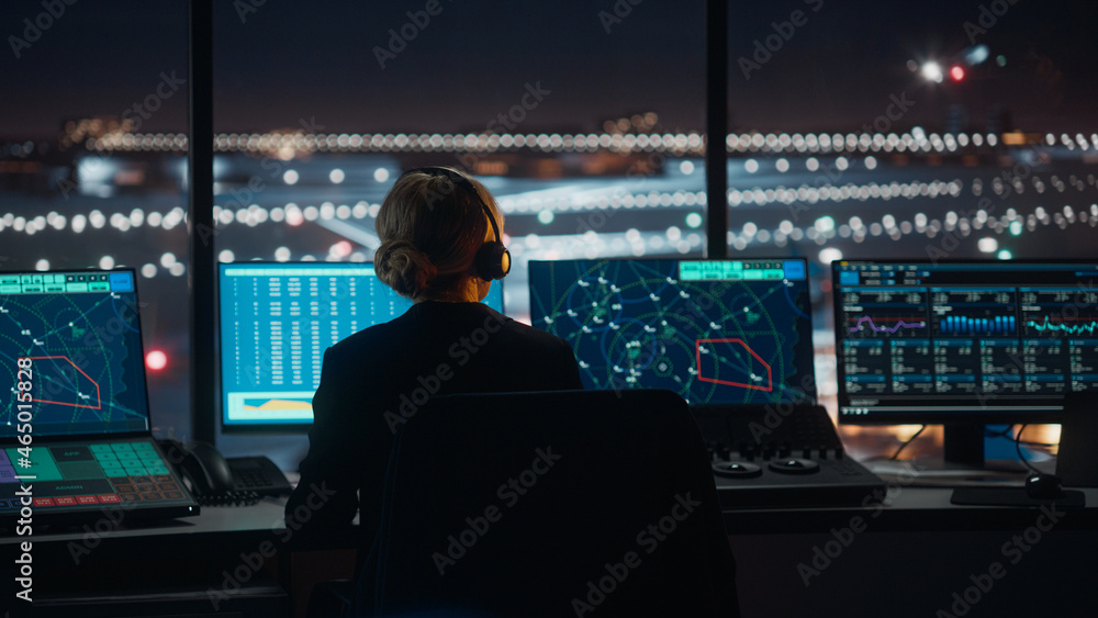 Female Air Traffic Controller with Headset Talk on a Call in Airport Tower at Night. Office Room is 