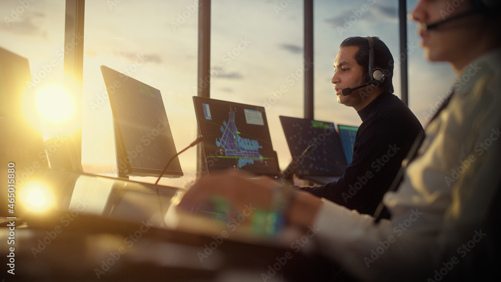 Male Air Traffic Controller with Headset Talk on a Call in Airport Tower. Office Room is Full of Des