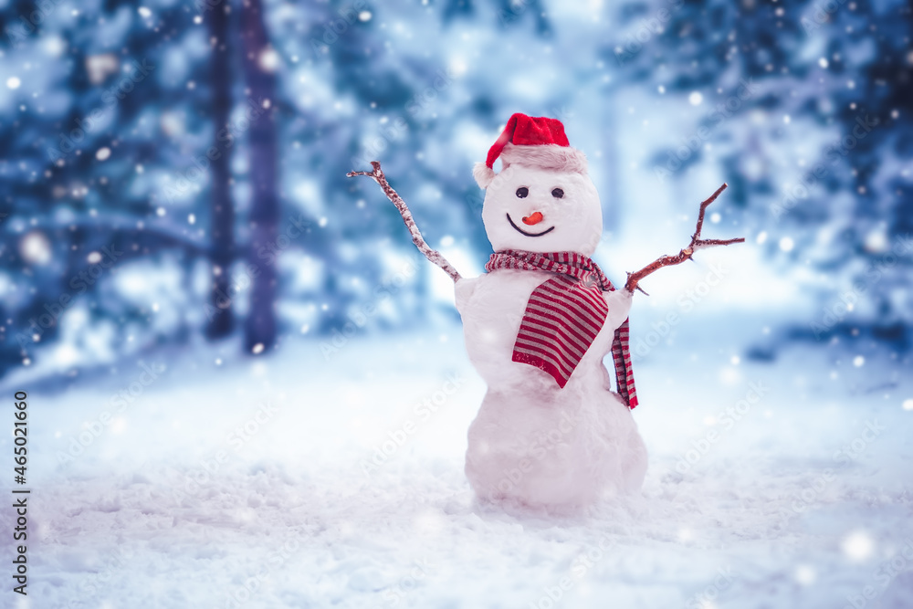 Cheerful snowman with striped scarf and in Christmas hat standing in winter forest.