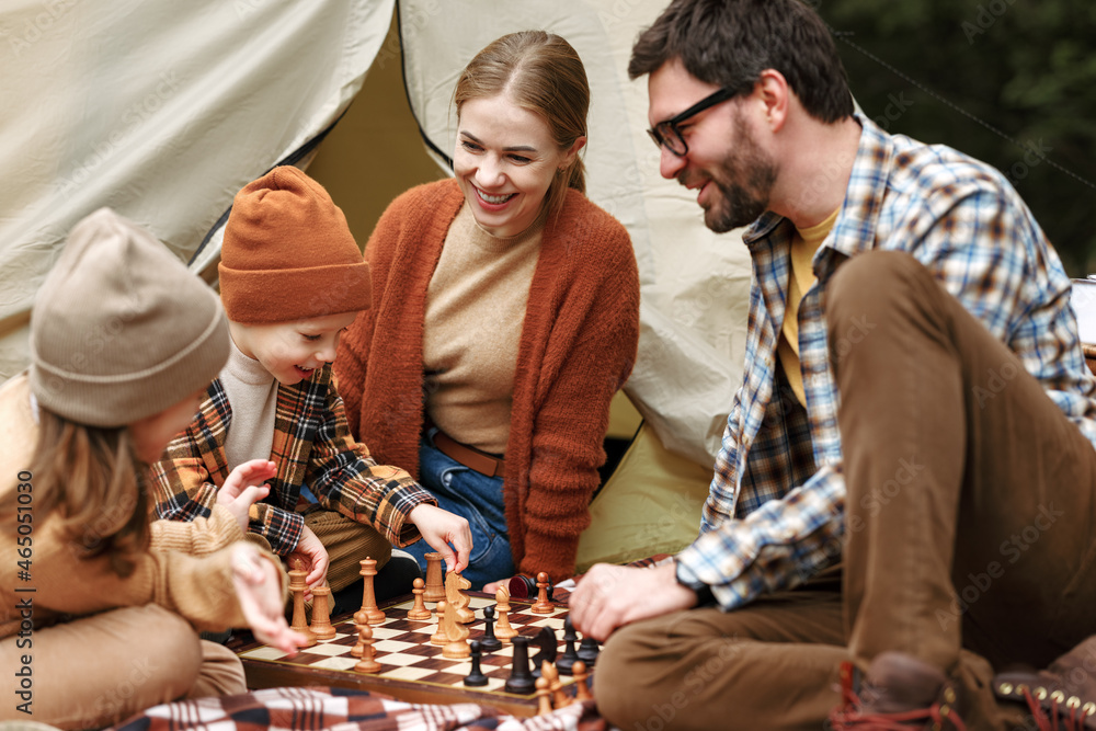 Happy smiling family playing chess game at campsite during camping trip in nature