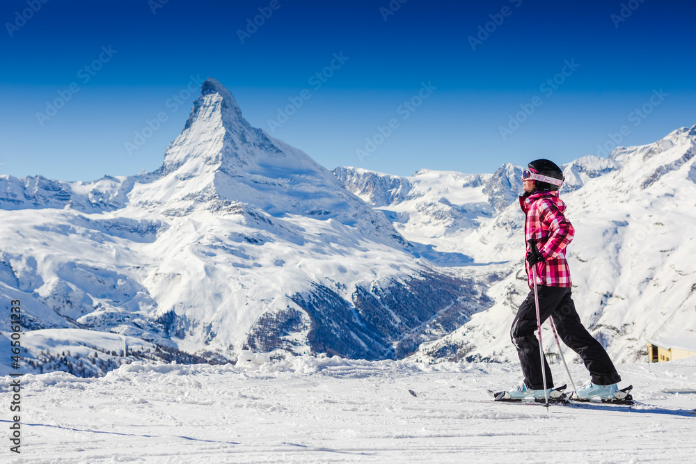 在阳光明媚的冬季，女滑雪者在山顶休息，在滑雪场观察大自然