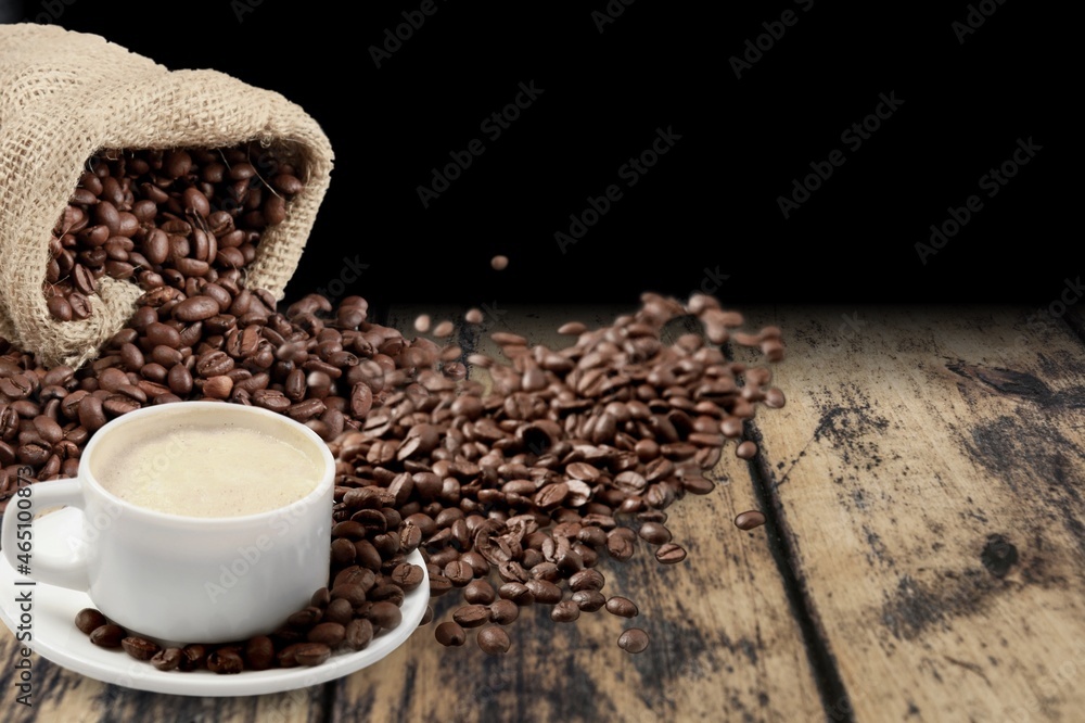 Hot coffee in a white coffee cup and many beans placed around