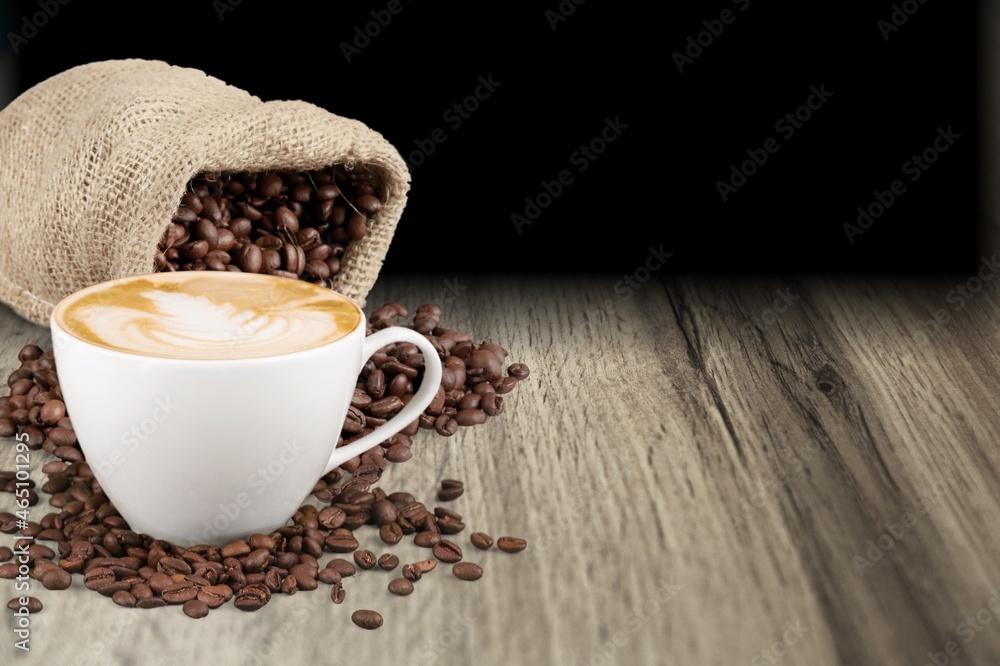 Hot coffee in a white coffee cup and many beans placed around