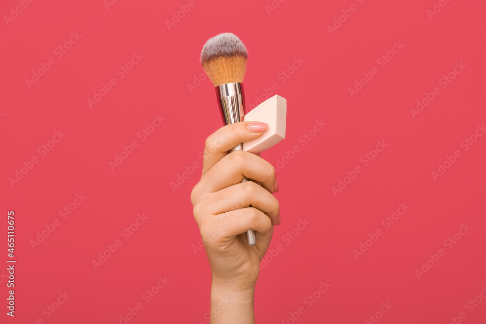 Female hand with stylish makeup sponge and brush on color background