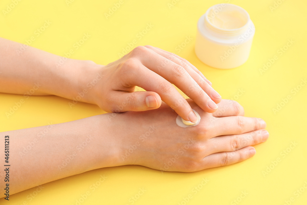 Woman applying hand cream on color background