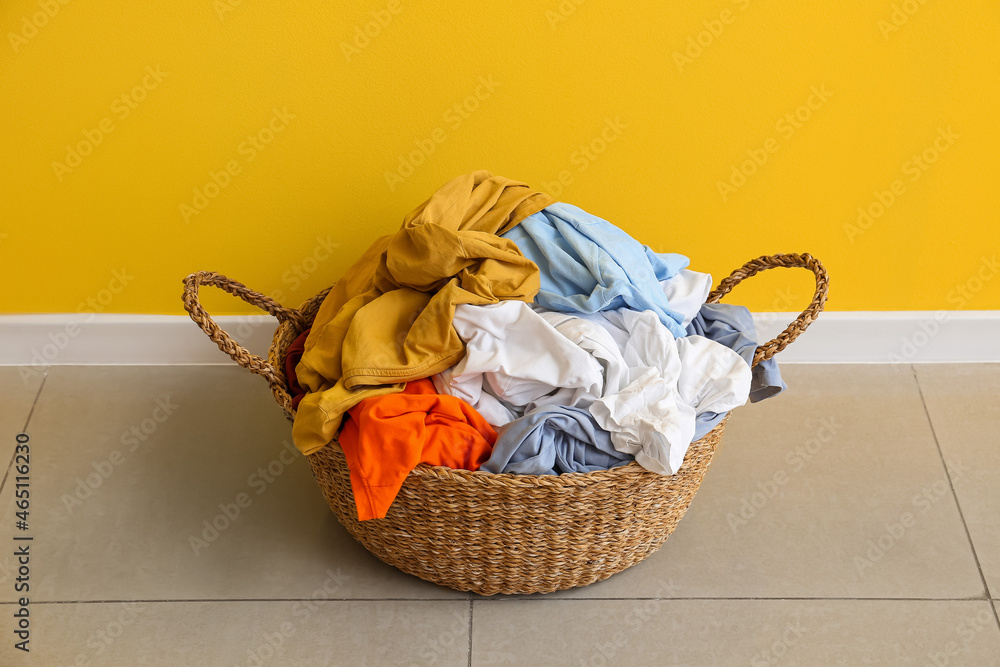 Wicker basket with laundry near yellow wall