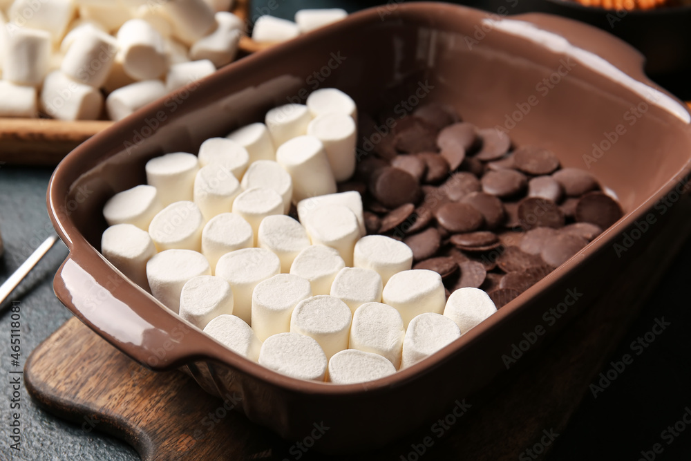 Baking dish with uncooked Smores dip on dark background, closeup