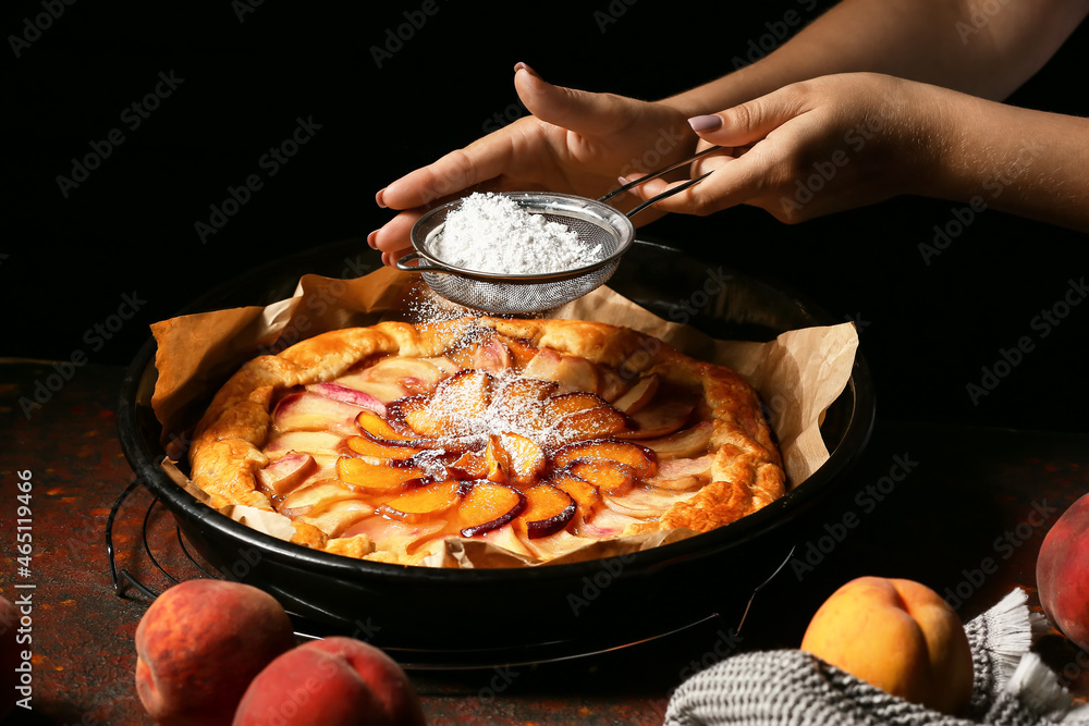 Woman sprinkling powdered sugar into tasty peach galette on table