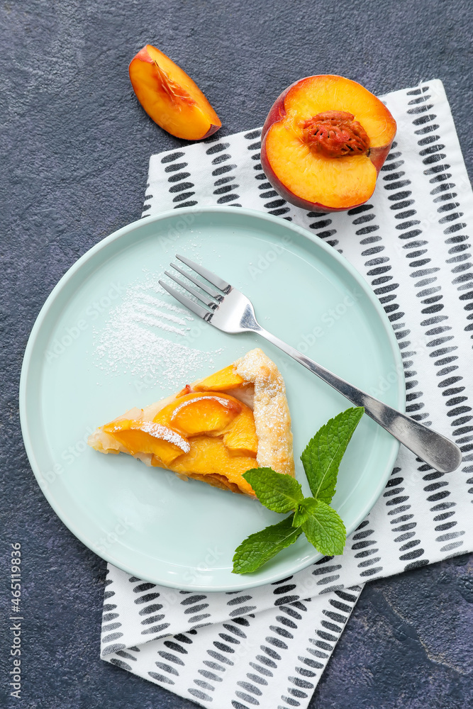 Plate with piece of tasty peach galette on dark background