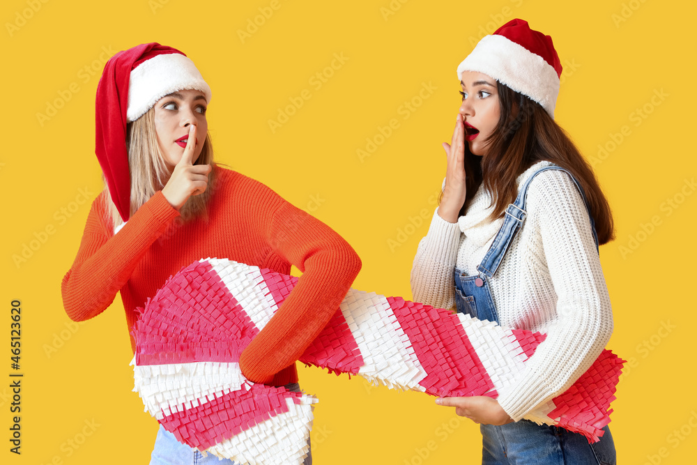 Young women with candy cane pinata on yellow background