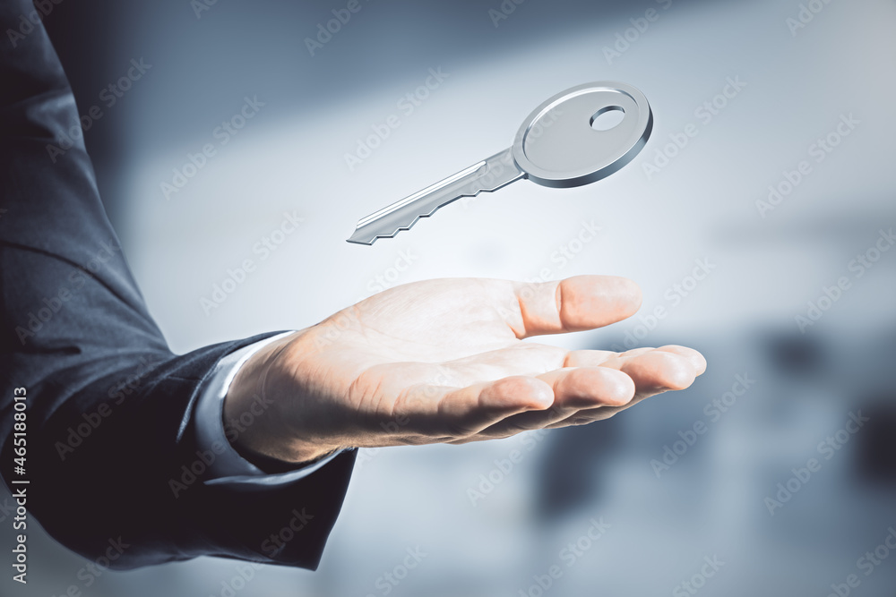 Close up of businessman hand holding silver key on blurry interior background. Mortgage and purchase