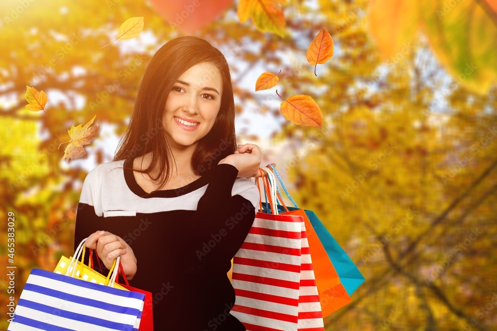 Happy elegant woman with shopping bags and autumn yellow background