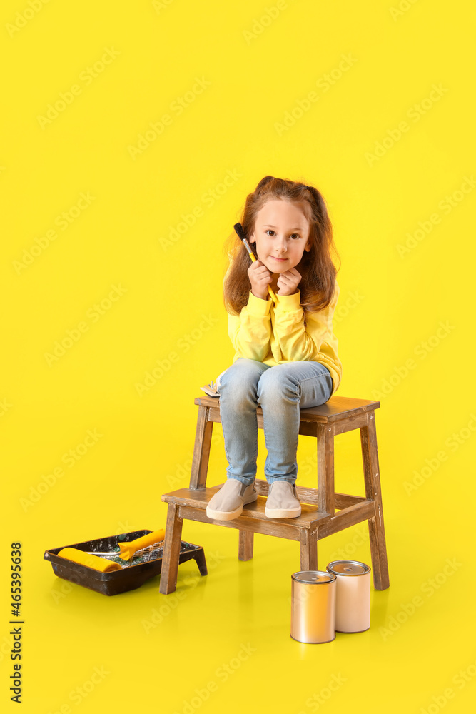 Cute little girl with paint brush on yellow background